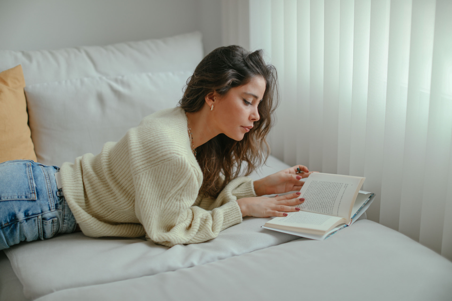 A person relaxing on a couch reading a book by a window